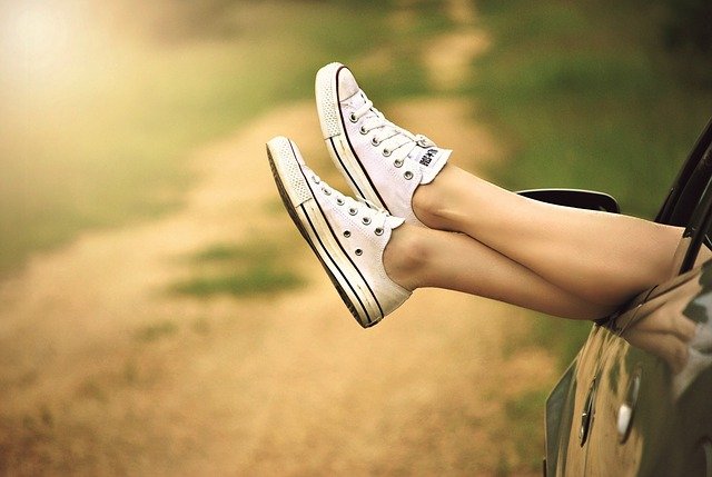 Legs popping out a car window wearing white sneakers