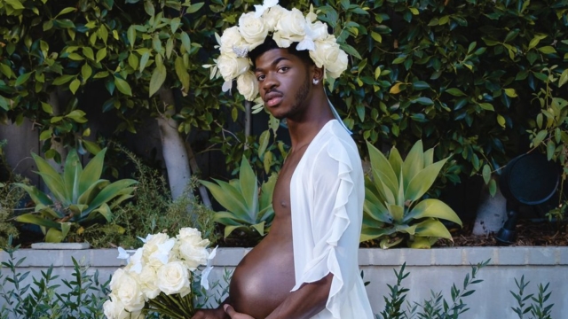 Photo of rapper Lil Nas X in a faux maternity shoot with him wearing a fake prosthetic bayb bump, a crown of white roses holding a bouquet of white roses in an article about celebrity round up